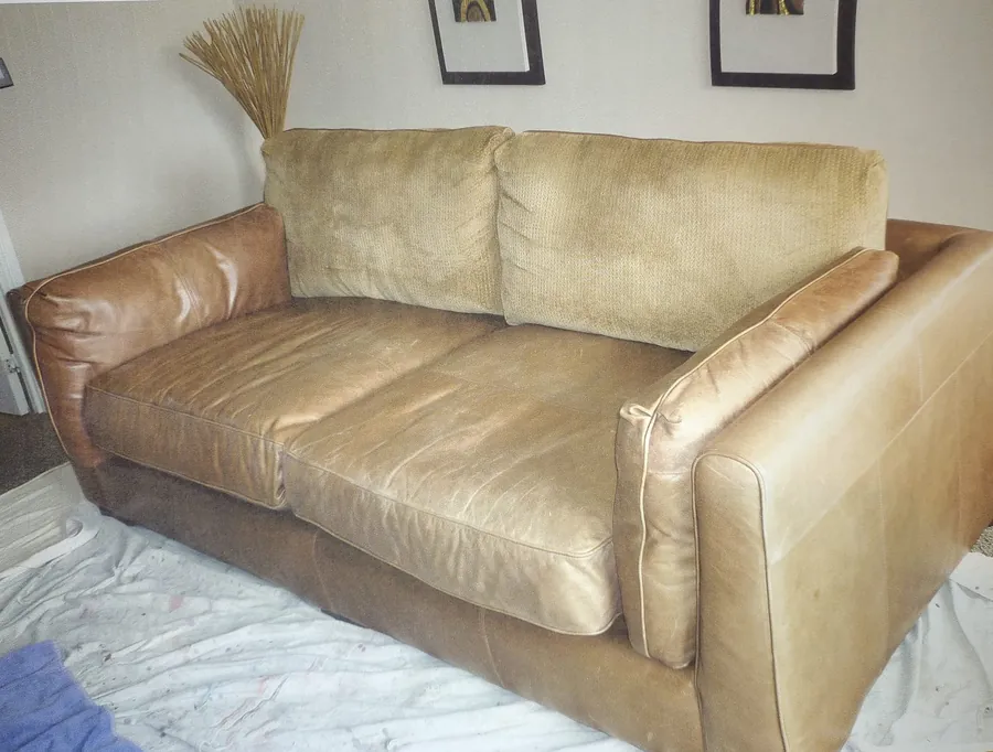Pale, faded leather sofa with fabric back cushions before restoration